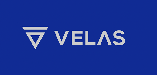 The image features the Velas logo with a stylised triangular symbol and the word "VELAS" in white against a blue background. (Captioned by AI)